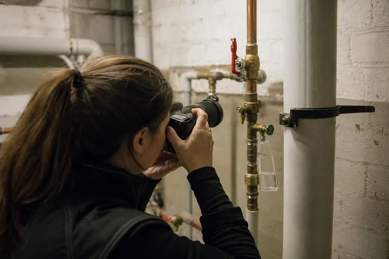 Technikerin fotografiert eine Probenahmestelle an einer Warmwasserleitung